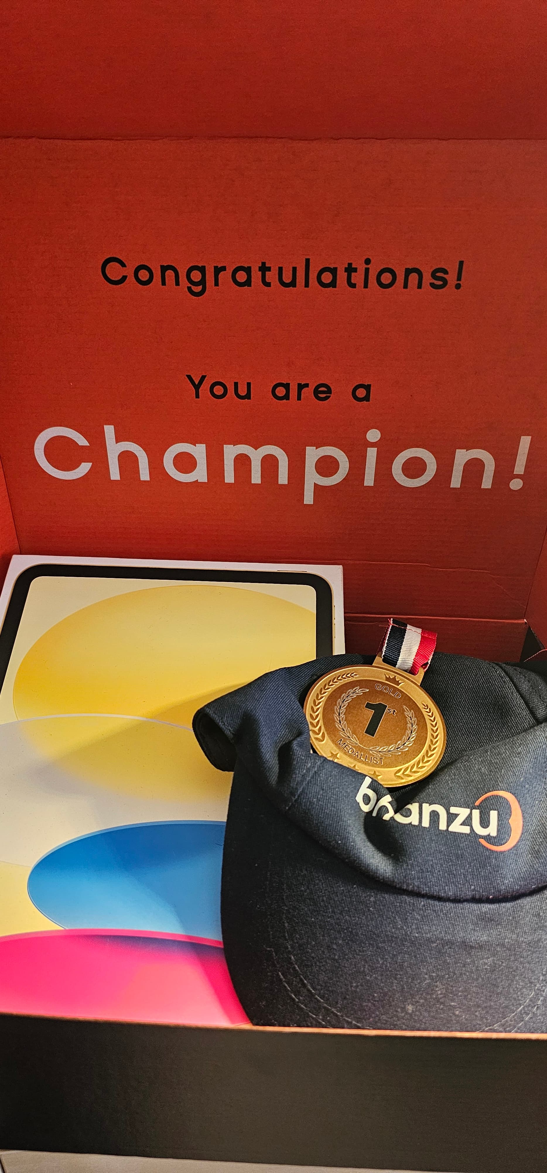 Red box with "Congratulations! You are a Champion!" text, gold medal, cap, and tablet box.