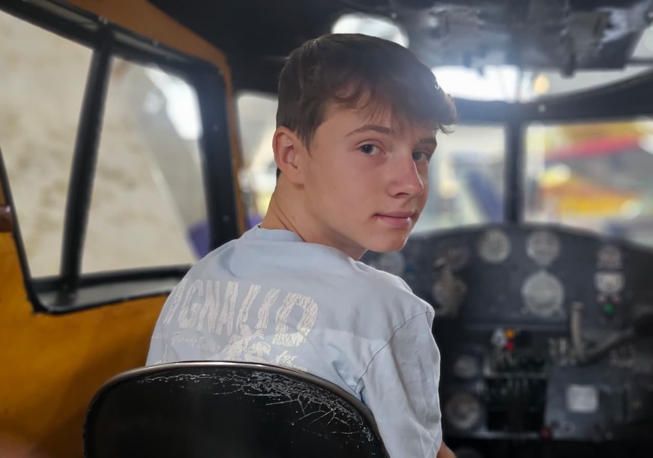 Young boy looks back over his shoulder while sitting in a vintage aircraft cockpit.