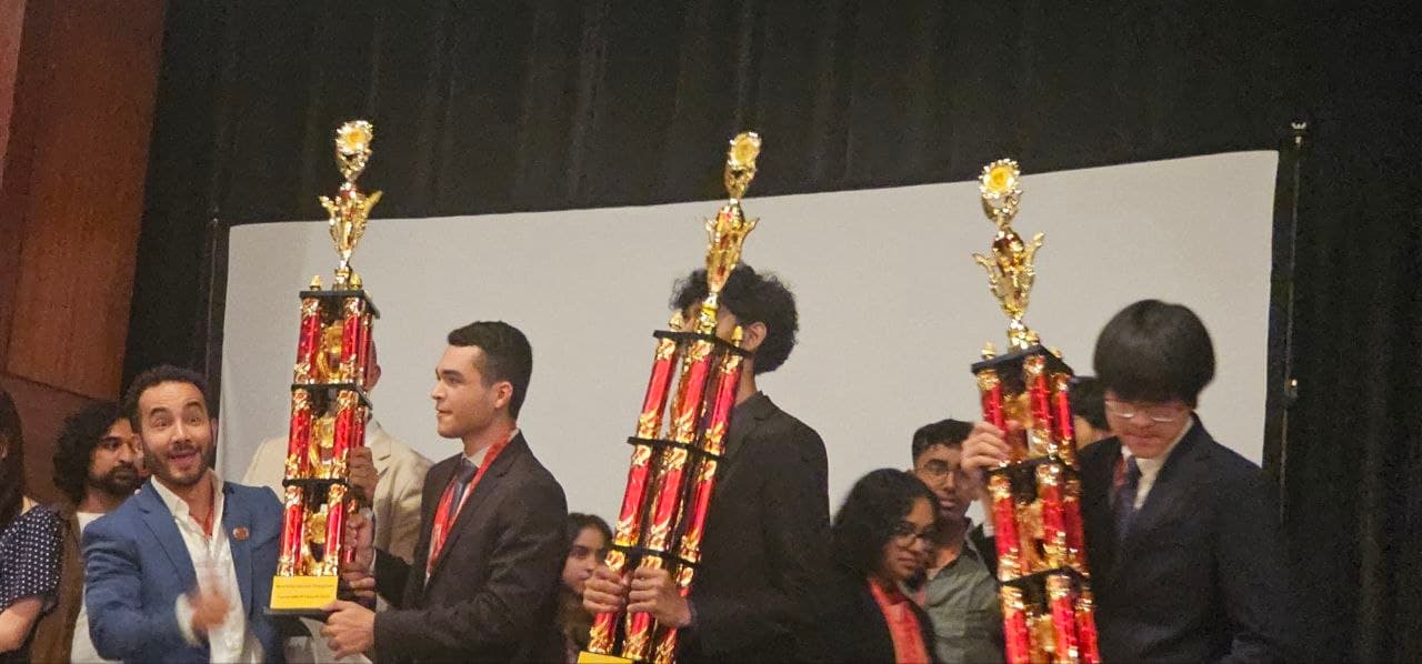 Young men in suits holding large red and gold trophies during an awards ceremony presentation.