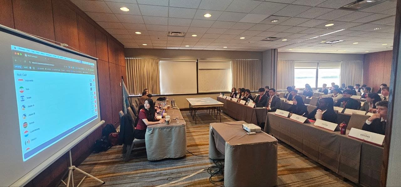 Students in suits attend a Model United Nations session with a roll call screen.