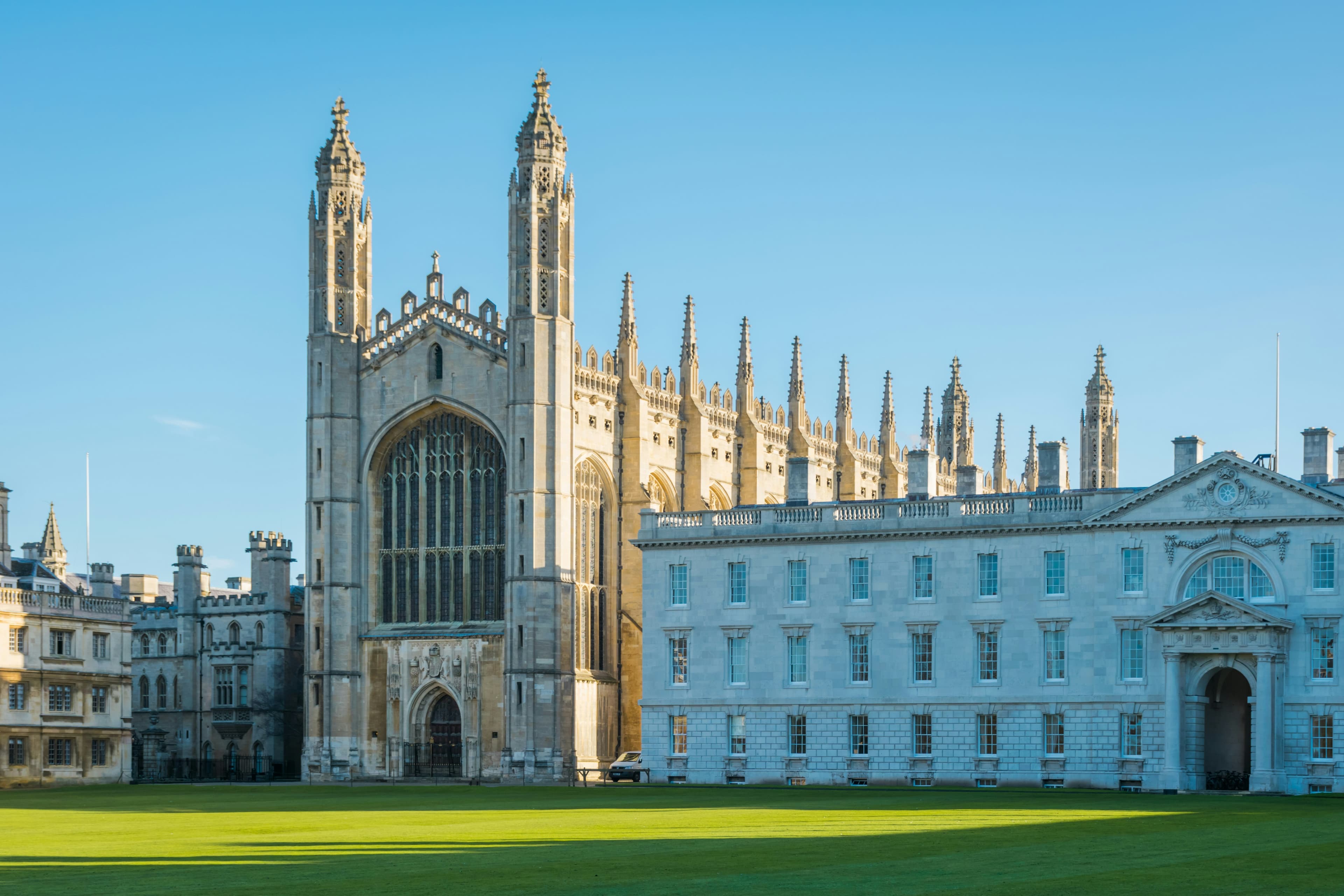 Gothic King's College Chapel and white neoclassical Gibbs Building overlook a manicured green lawn.