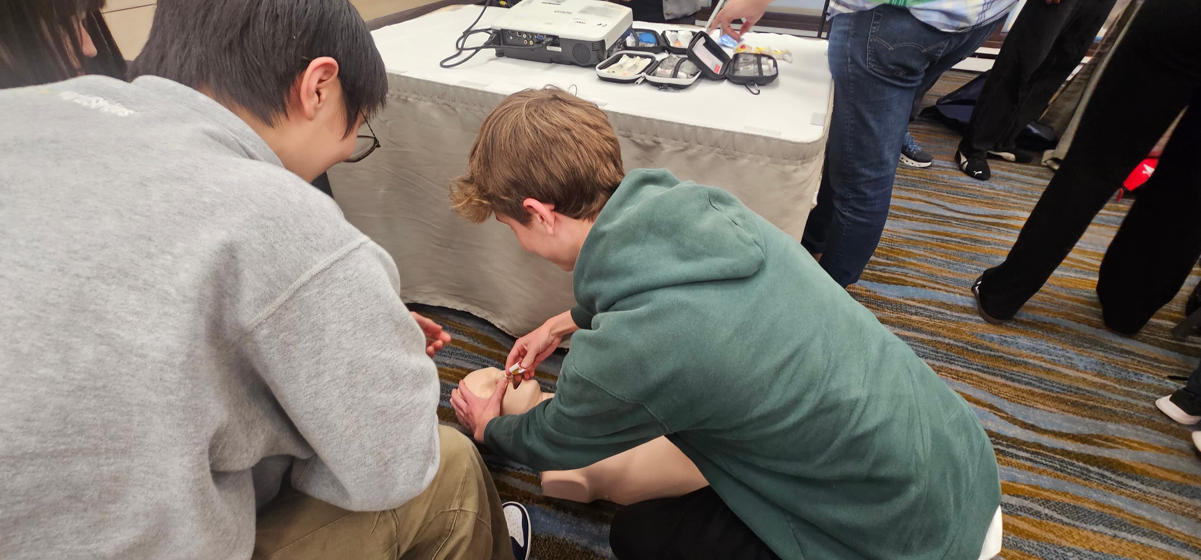 Two students practice medical procedures on a CPR manikin during a training workshop.